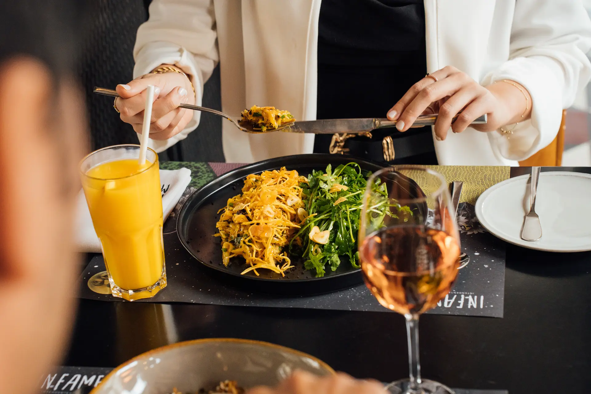 Duas pessoas à mesa a partilhar pratos, com sumo de laranja e um copo de vinho rosé